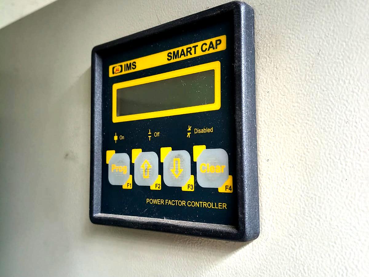 Controlador automático de fator de potência instalado na parede da cabine, com display e teclas de programação